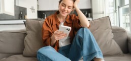 Woman resting on couch reading messages on mobile phone.